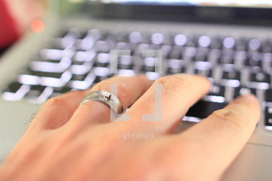 cross on a wedding band and hand on a keyboard 