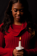 Reverent woman holding a lit candle, in prayer with her head bowed.