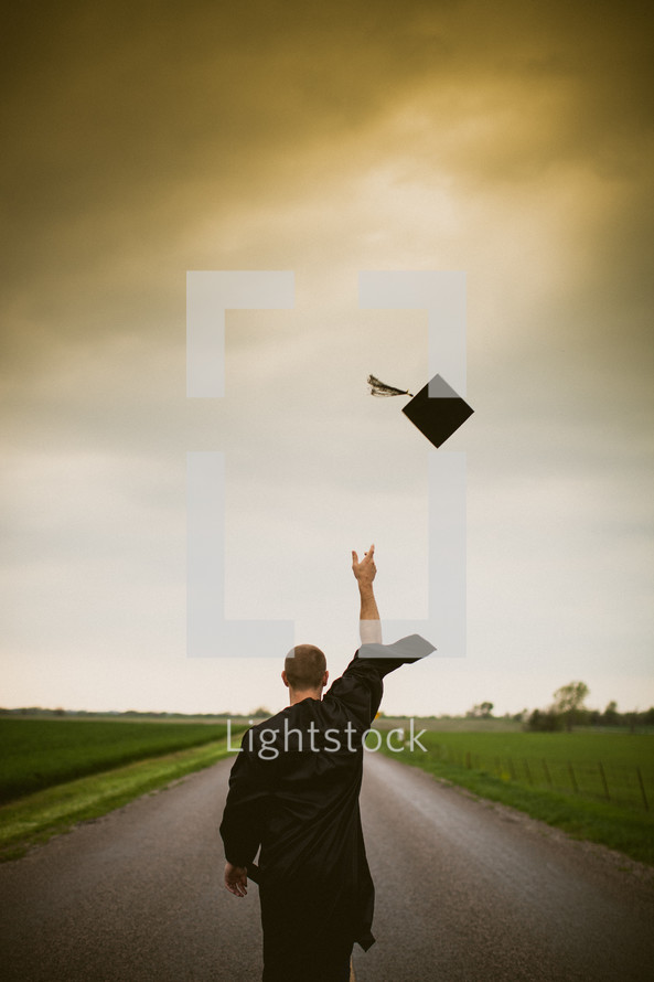 Graduate tossing cap in the air while walking down the middle of the road.