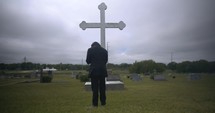 Young man in black suit looking at cross praying in worship in cinematic slow motion.