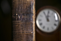 spine of an old leather Bible and clock on a desk 