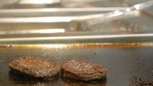 Hamburger patties cooking on a restaurant stove top.