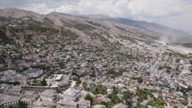 Drone flyover Gjirokaster cityscape with massive mountains in Background, Albania