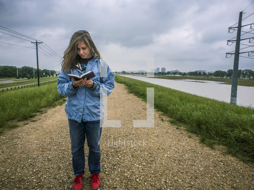 A woman reading in the middle of a gravel road.