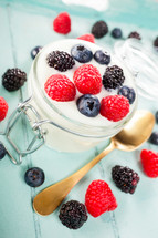 Jar of yogurt and berries on a light blue wooden tray