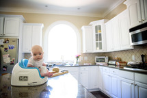 an infant in a Bumbo seat on a kitchen countertop 