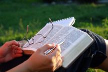 person sitting outdoors in grass reading a Bible 