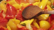 red and yellow peppers cooking in a pan, stirring with wooden spoon
