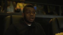 African American man sitting in armchair watching a horror movie at the cinema, scary face.