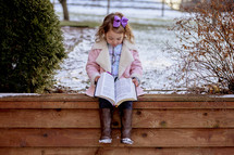 girl in a pink coat reading a Bible 