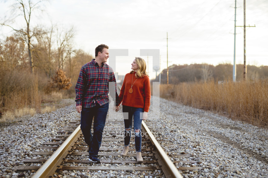 couple holding hands walking down the middle of train tracks 