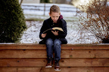a child reading a Bible outdoors in winter 