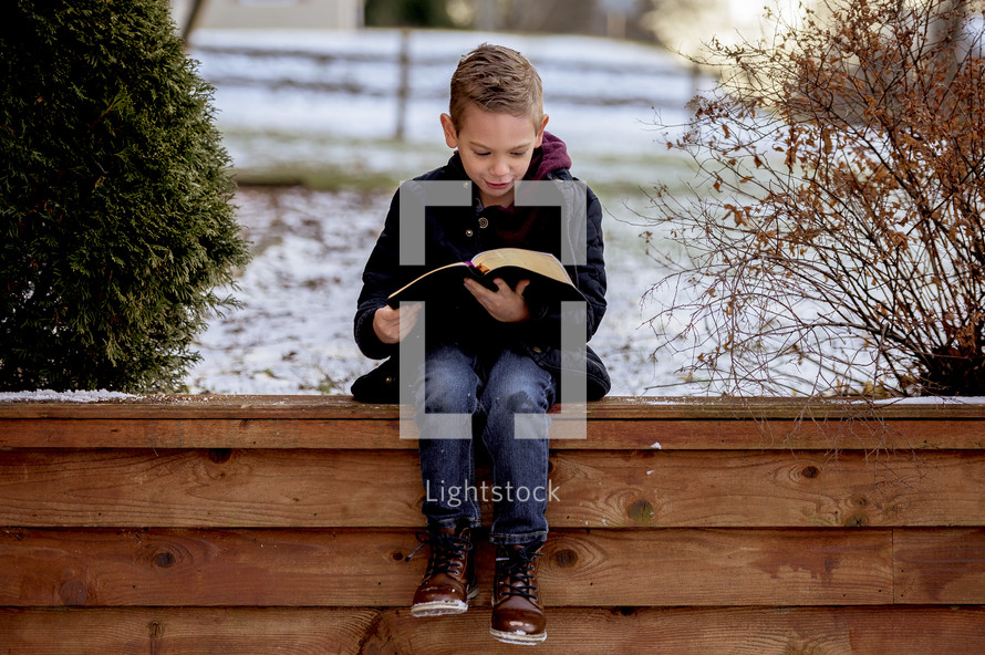 a child reading a Bible outdoors in winter 