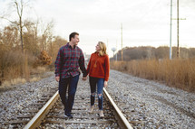 couple holding hands walking down the middle of train tracks 