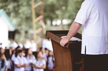 man at a podium in front of school children 