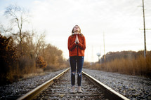 a woman praying standing in the middle of train tracks 
