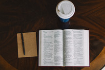 pen, notepad, open Bible, and coffee cup on a table 