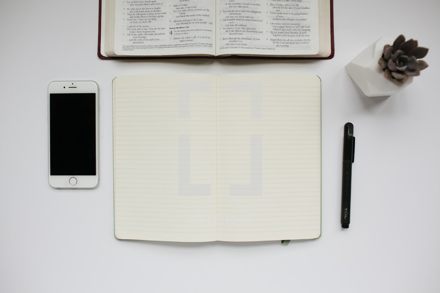 open Bible, journal, pen, succulent plant, and cellphone on a white background 