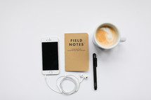 earbuds, iPhone, field notes book, latte, and pen 
