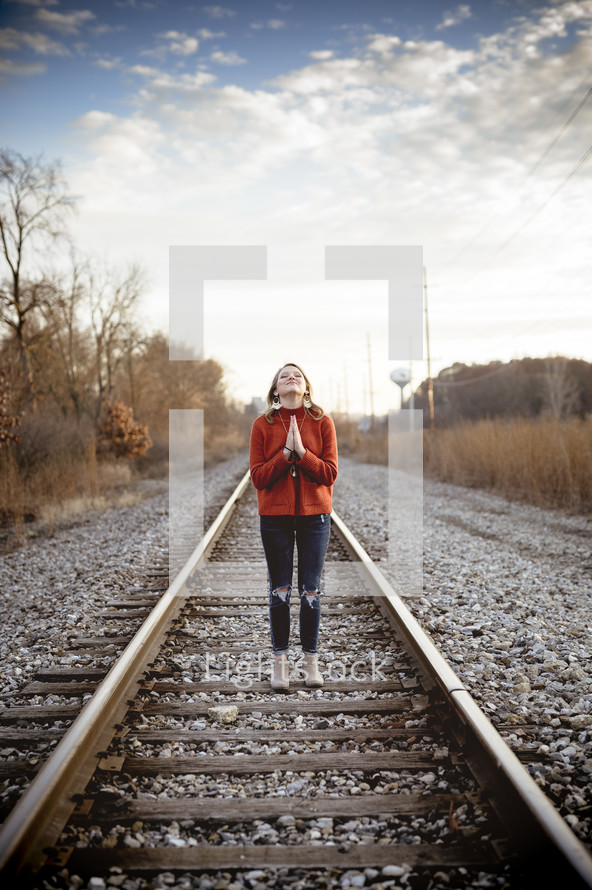 woman praying standing in the middle of train tracks 