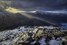 rays of sunlight shining on a mountain top and snow on rocks 