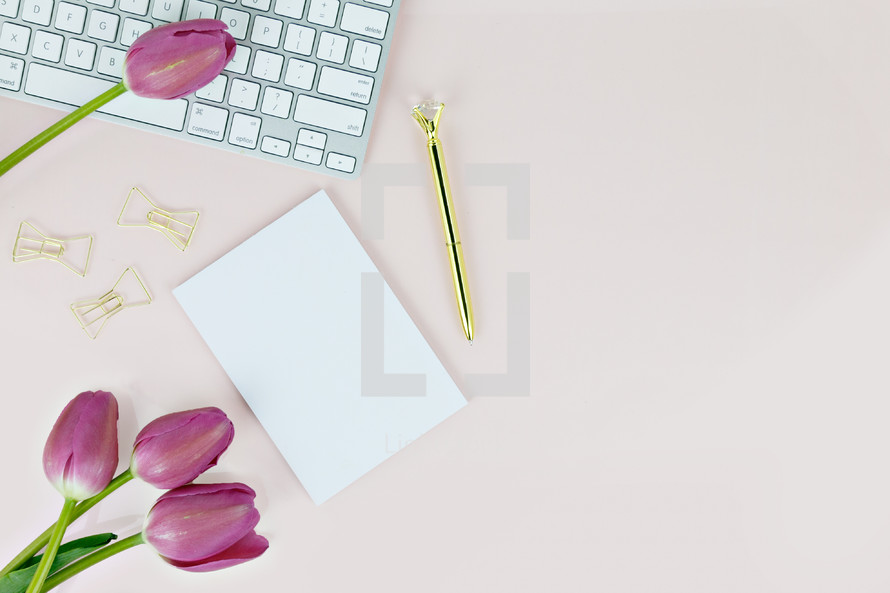 pen, white paper, gold paperclips, and fuchsia tulips on a pink background 