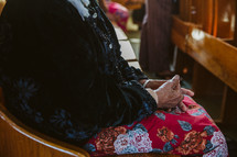 elderly woman sitting in a church pew praying 