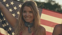 young woman walking with an American flag draped over their backs 