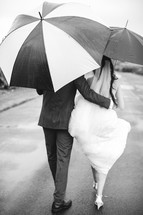bride and groom walking with umbrellas 