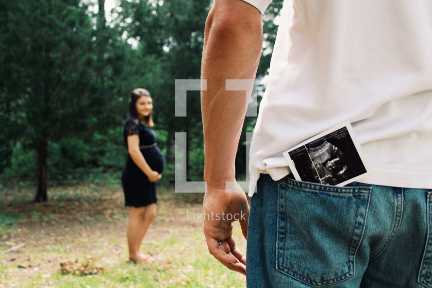 a pregnant woman and a picture of a sonogram in fathers pocket 