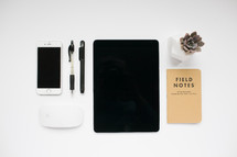 iPhone, iPad, computer mouse, field notes book, succulent plant, and pens 
