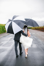 bride and groom walking carrying umbrellas 