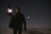 a man holding a lantern outdoors at night 