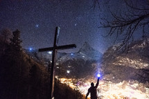 cross and man shining a flashlight and mountains 