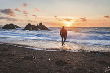 man walking on a beach at sunset in a coat 