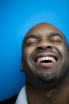 A man with his head thrown back and laughing against a blue background.