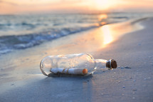 Message in a bottled washed up on shore at sunset.