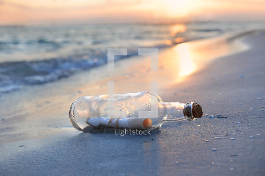 Message in a bottled washed up on shore at sunset.