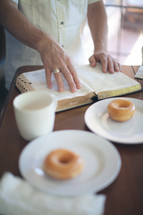 Man's hands on an open Bible at the breakfast table.