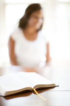 open Bible and a blurry image of a woman in the background