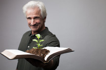 man holding a Bible with a plant growing from its pages 