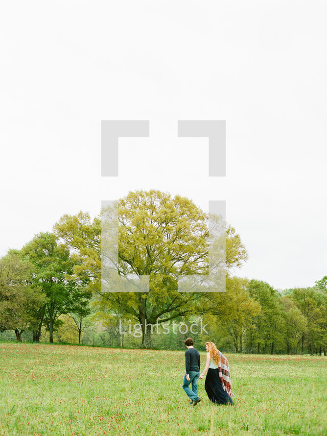 Couple walking through a field with trees.
