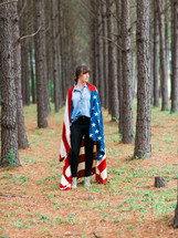 woman wearing an American flag standing in a forest 