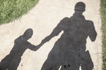 Shadow of man holding his son's hand on a sidewalk.