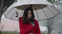 Wet girl standing in the cold rain holding an umbrella