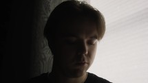 Young white man looking for satisfaction and hope. He is questioning his life in his dimly lit bedroom. The moody cinematic atmosphere, adds tension and mystery. 