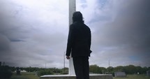 Young man in black suit looking at cross praying in worship in cinematic slow motion.