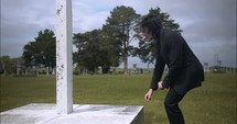 Young man kneeling in black suit looking at cross praying in worship in cinematic slow motion.