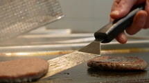 Cooking flipping hamburger patties on a restaurant stovetop.