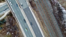 Aerial top shot of Gardiner Expressway in Toronto on a winter day. The drone moves forward as it shows the pass of cars across the highway. Railroad tracks are visible on the right side of the traffic